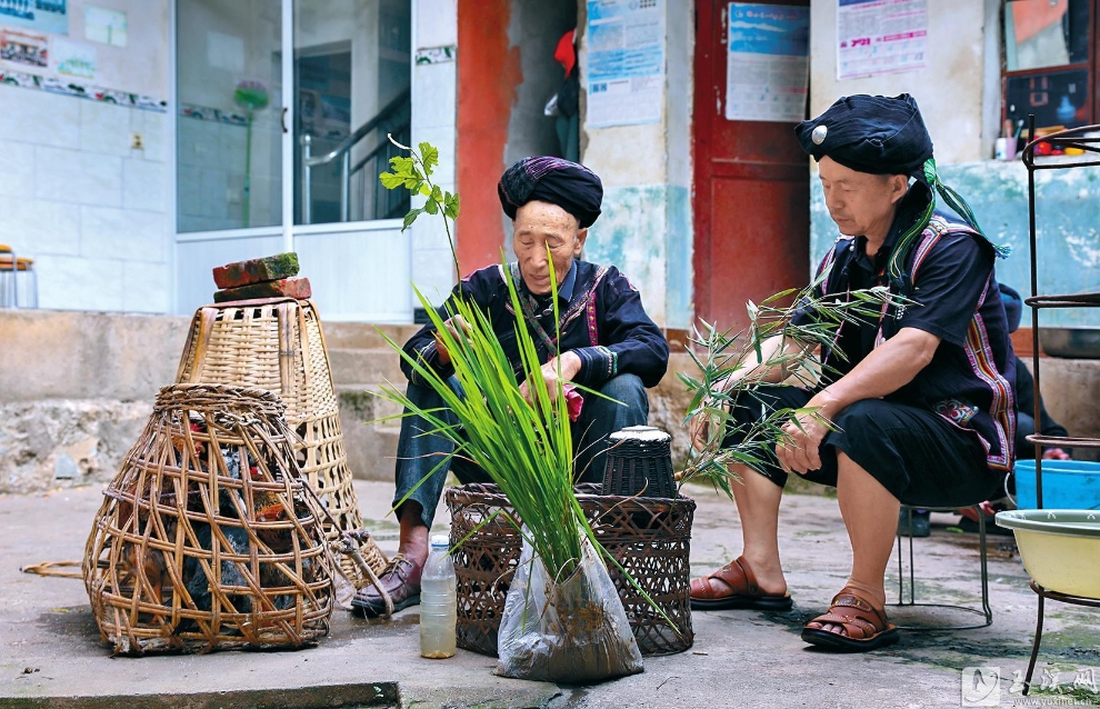 摩批（左）坐在主人家门口念经祈福。